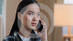 Sad asian woman millennial confused angry girl indoors talking on phone answering call worries about bad news network