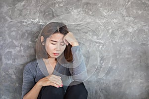 Sad Asian woman sitting alone against the wall feeling depressed and lonely