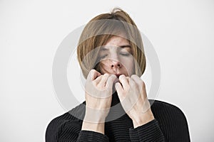 Sad attractive woman is pulling up pullover collar, eyes closed. Lifestyle concept.