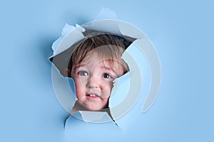 Sad baby in a hole on a paper blue background. Torn child\'s head studi