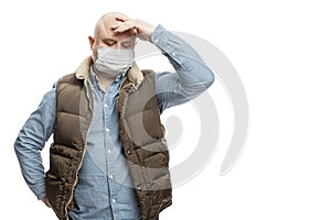 Sad bald adult man in a medical mask stands holding his head with his hand. Precautions quarantined for the period of the