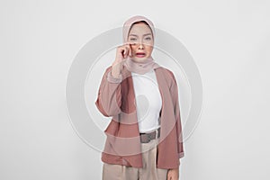 Sad beautiful Asian Muslim woman in hijab crying and wiping tears on cheek over isolated white background