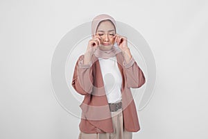 Sad beautiful Asian Muslim woman in hijab crying and wiping tears on cheek over isolated white background