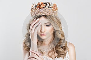 Sad Beautiful blonde girl in a golden crown on white grey background, eyes closed looking down with grief hand on shoulder pink