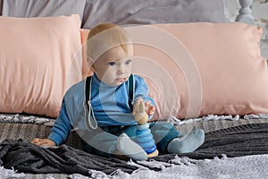 Sad, but beautiful blue-eyed baby sitting on the bed next to the toy pyramid