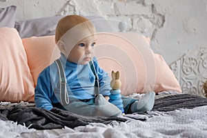 Sad, but beautiful blue-eyed baby sitting on the bed next to the toy pyramid