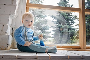 Sad, but beautiful blue-eyed baby sitting on the windowsill and looking at the camera
