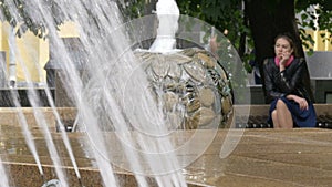 A sad beautiful girl sits in a park, near a fountain. Bad news, hopelessness and longing.