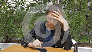 Sad beautiful girl sitting at a table in a cafe. Reads sms on a smartphone. Sadness and longing, hopelessness. Close-up