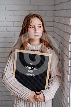 Sad beautiful woman holding felt letter board with the words Someone You Loved