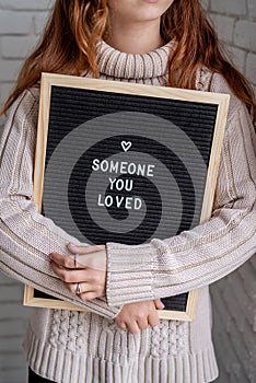 Sad beautiful woman holding felt letter board with the words Someone You Loved