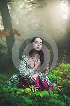 Sad beautiful woman in medieval dress sitting in grass