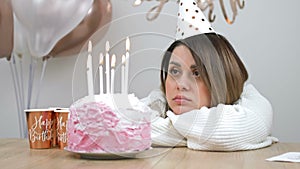 Sad birthday. Beautiful girl sits alone in front of a birthday cake.