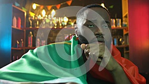 Sad black fan holding flag of Portugal in bar, upset about sports team defeat