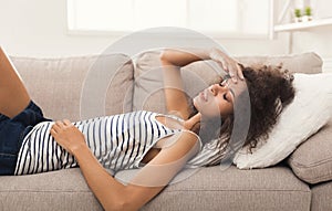 Sad black girl feeling pain lying on sofa