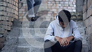 Sad black teenager sitting on stairs in gateway, problem of bullying at school