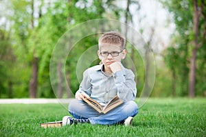 Sad boy with book on green grass
