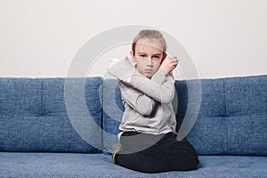 Sad boy with broken hand at home. Kid with broken arm and gypsum sitting on the sofa