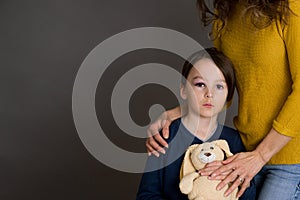 Sad boy with bruised eye, hugging mom and teddy bear at home