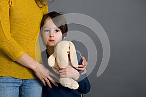 Sad boy with bruised eye, hugging mom and teddy bear at home