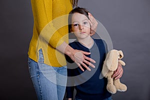 Sad boy with bruised eye, hugging mom and teddy bear at home