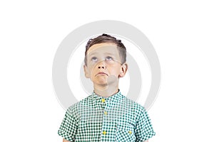 A sad boy with a crooked mouth in a green shirt looks up somewhere. A beautiful child with a sad expression. White background. Iso