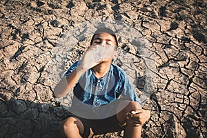 Sad boy drinking water on crack ground