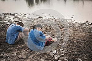 Sad boy and girl sitting on cracked dry ground