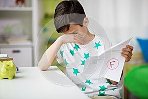 Sad boy holding school test with f grade