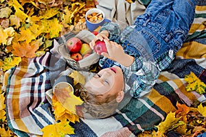 A sad boy lies on a blanket with an Apple in his hands in an autumn Park. There are a lot of yellow maple leaves around. Picnic in