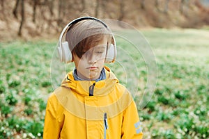 Sad boy listening to music at nature. Kid with headphones relaxing in the spring park