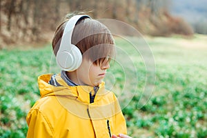 Sad boy listening to music at nature. Kid with headphones relaxing in the spring park