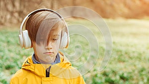 Sad boy listening to music at nature. Kid with headphones relaxing in the spring park