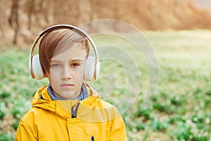 Sad boy listening to music at nature. Kid with headphones relaxing in the spring park. Upset boy with headphones on the walk