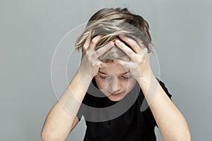 The sad boy sits at the table and has his head in his hands. Loneliness and stress. Grey background. Close-up