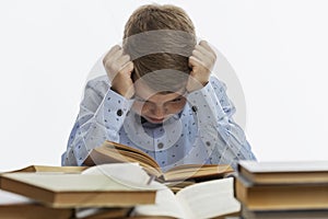 Sad boy sits at a table with many books. A child of 9-10 years old in a blue shirt clasped his head in his hands. White background