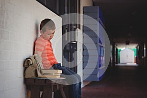 Sad boy sitting on bench by wall in corridor