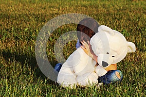 Sad boy sitting outdoors and hugging teddy bear