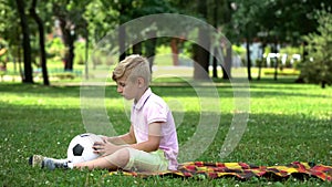 Sad boy sitting in park with football, lack of friends, victim of bullying