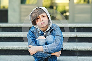 Sad boy is sitting on the stairs, before school. Alone unhappy child in city street. Bullying, depression, child protection or