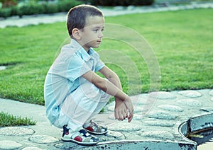 A sad boy is sitting on the street alone. Unhappy lonely child. Blue tone
