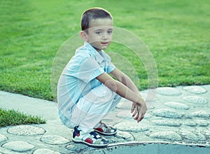 A sad boy is sitting on the street alone. Unhappy lonely child. Blue tone