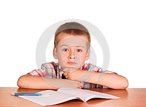 Sad boy sitting at table on notebook, pen isolated.