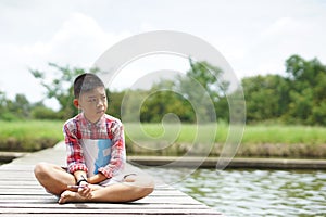 Sad a boy sitting thinking on wooden bridge in the garden.