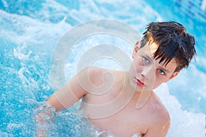 A sad boy standing in the pool in the summer in the chest in the water. He was not fun because he was already tired of swimming