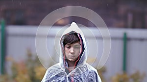 Sad boy standing in the rain with a raincoat, expressing pain on his face