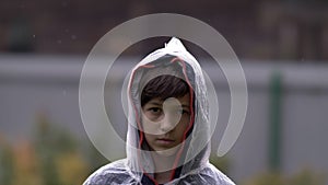 Sad boy standing in a raincoat in the rain