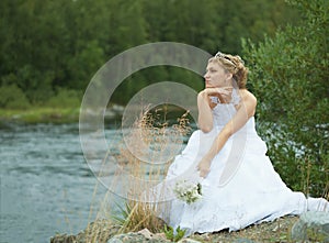 Sad bride sits on river bank