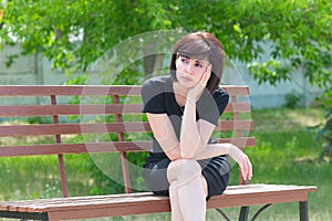 A sad brunette 35-40 years old sits on a bench with her chin propped
