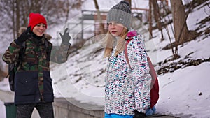 Sad bullied teen schoolgirl standing on winter day outdoors as rude schoolboy laughing gesturing sneering at background